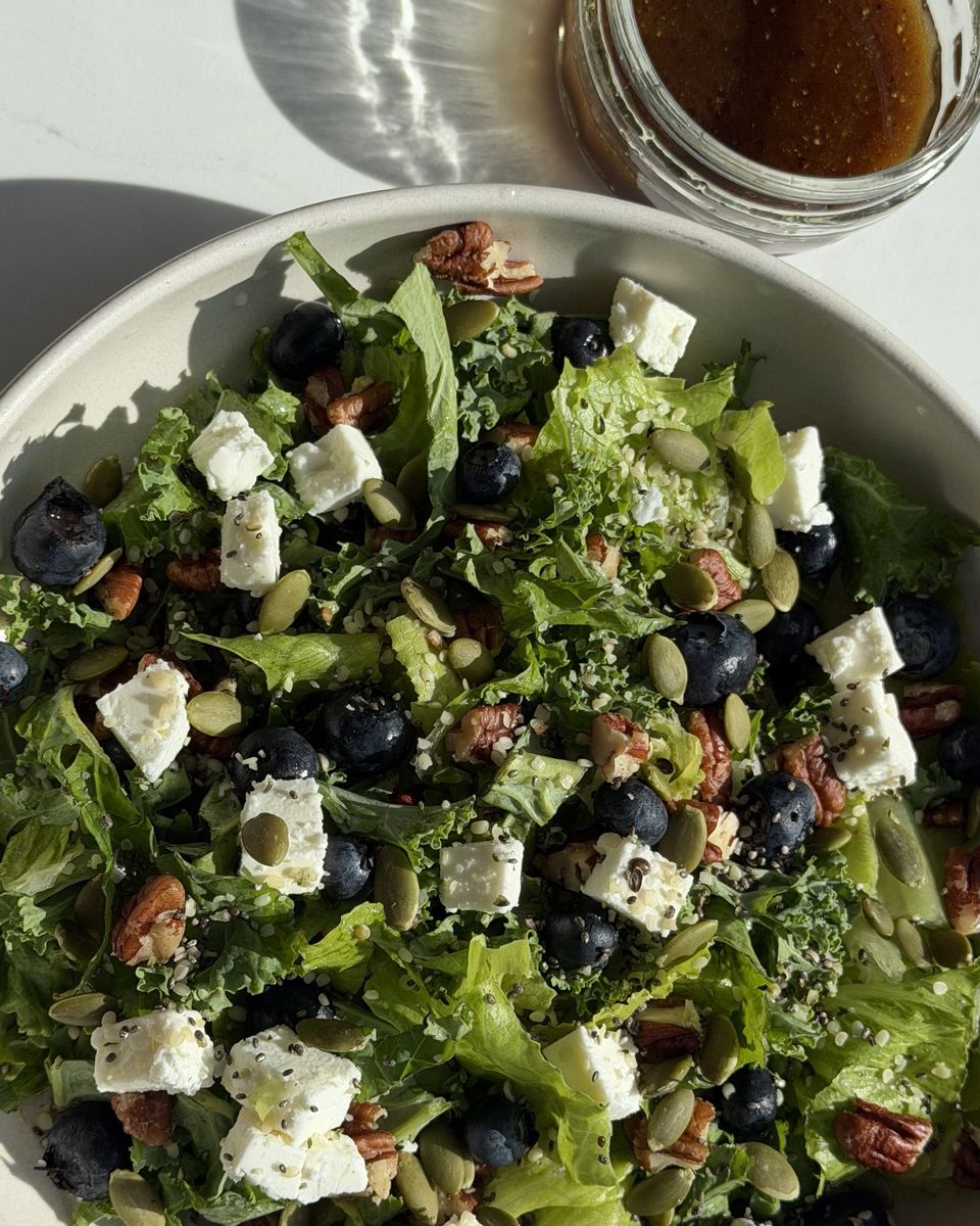 Kale salad with feta, blueberries, pecans and seeds, with a jar of dressing